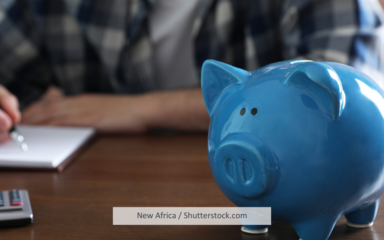 Ein blaues Sparschwein, im Hintergrund ein Mann, der Notizen macht