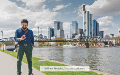 Ein Mann schaut auf sein Handy, im Hintergrund die Frankfurter Skyline