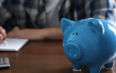 Ein blaues Sparschwein, im Hintergrund ein Mann, der Notizen macht