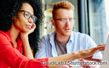 Eine Frau in roter Bluse deutet auf einen Laptop. Ein Mann neben ihr folgt ihren Erklärungen.