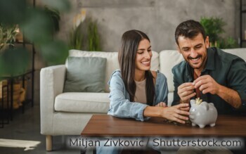 Eine Frau und ein Mann sitzen im Wohnzimmer vor dem Couchtisch, vor ihnen auf dem Tisch steht ein Sparschwein.