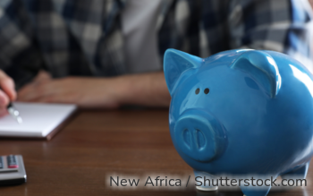 Ein blaues Sparschwein, im Hintergrund ein Mann, der Notizen macht